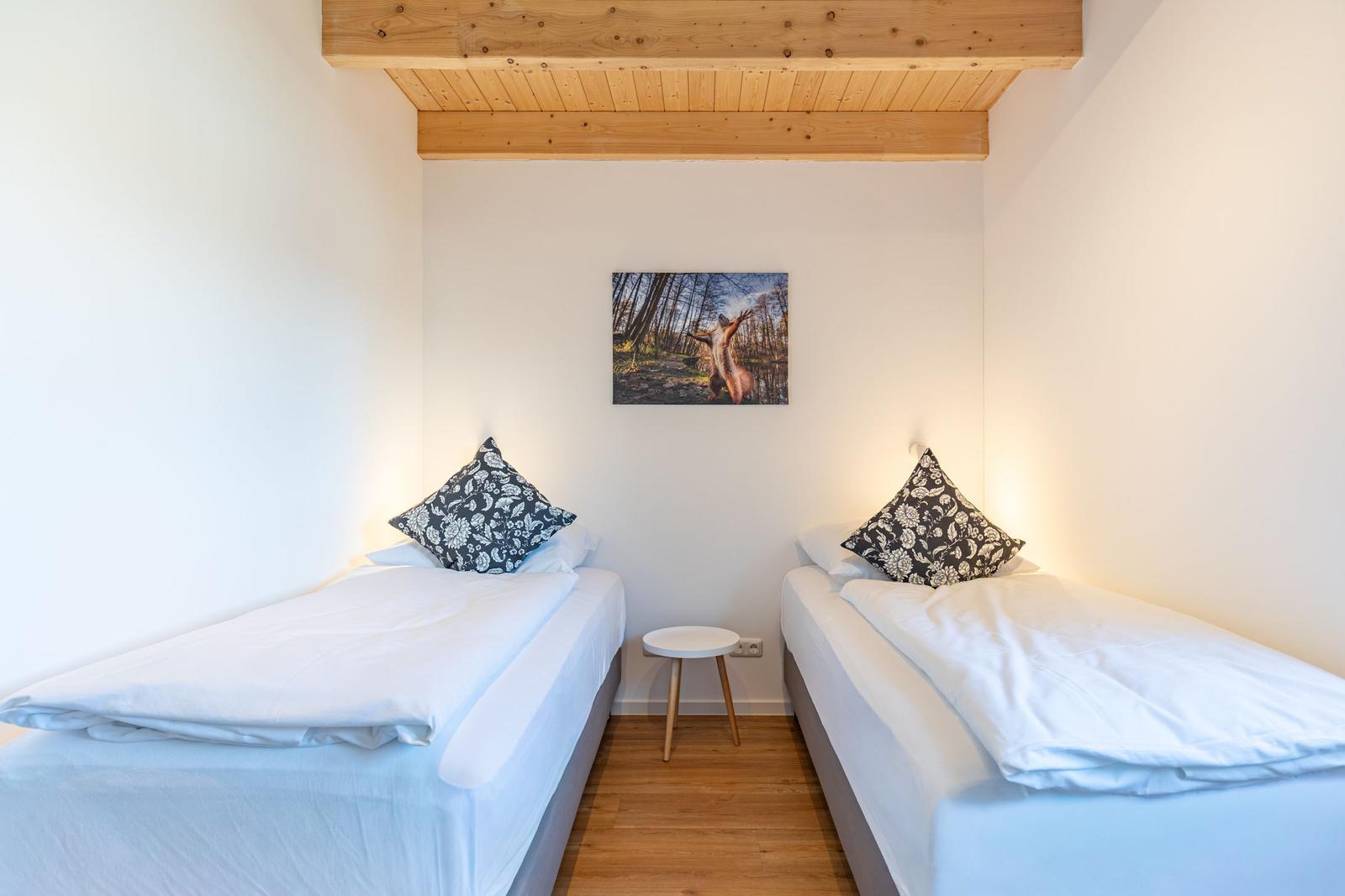 Zwei Betten mit weißen Bettwäschen und Kissen. Holzdecke und Wandbild.