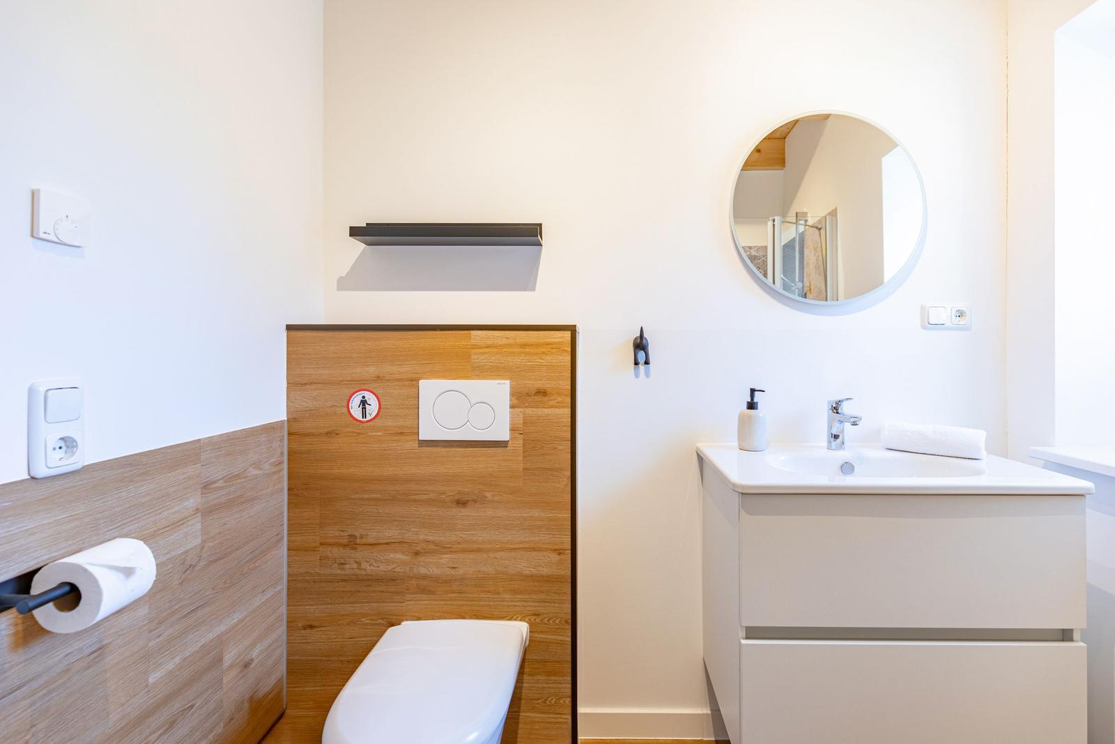 Badezimmer mit Toilette, Waschbecken und runden Spiegel