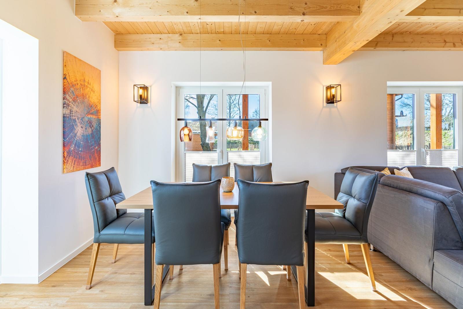 Essbereich mit Tisch, Stühlen und Sofa. Holzdecke und Wandbild sichtbar.