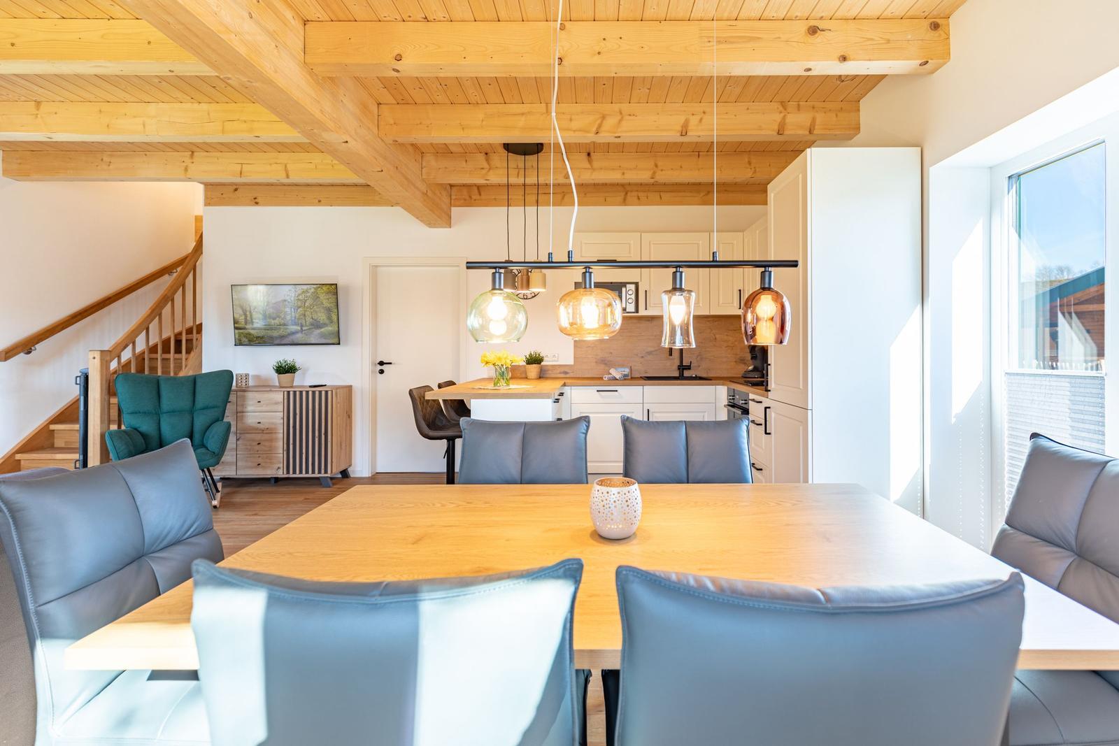 Essbereich mit Holztisch und Stühlen, Küche und Treppenhaus im Hintergrund.