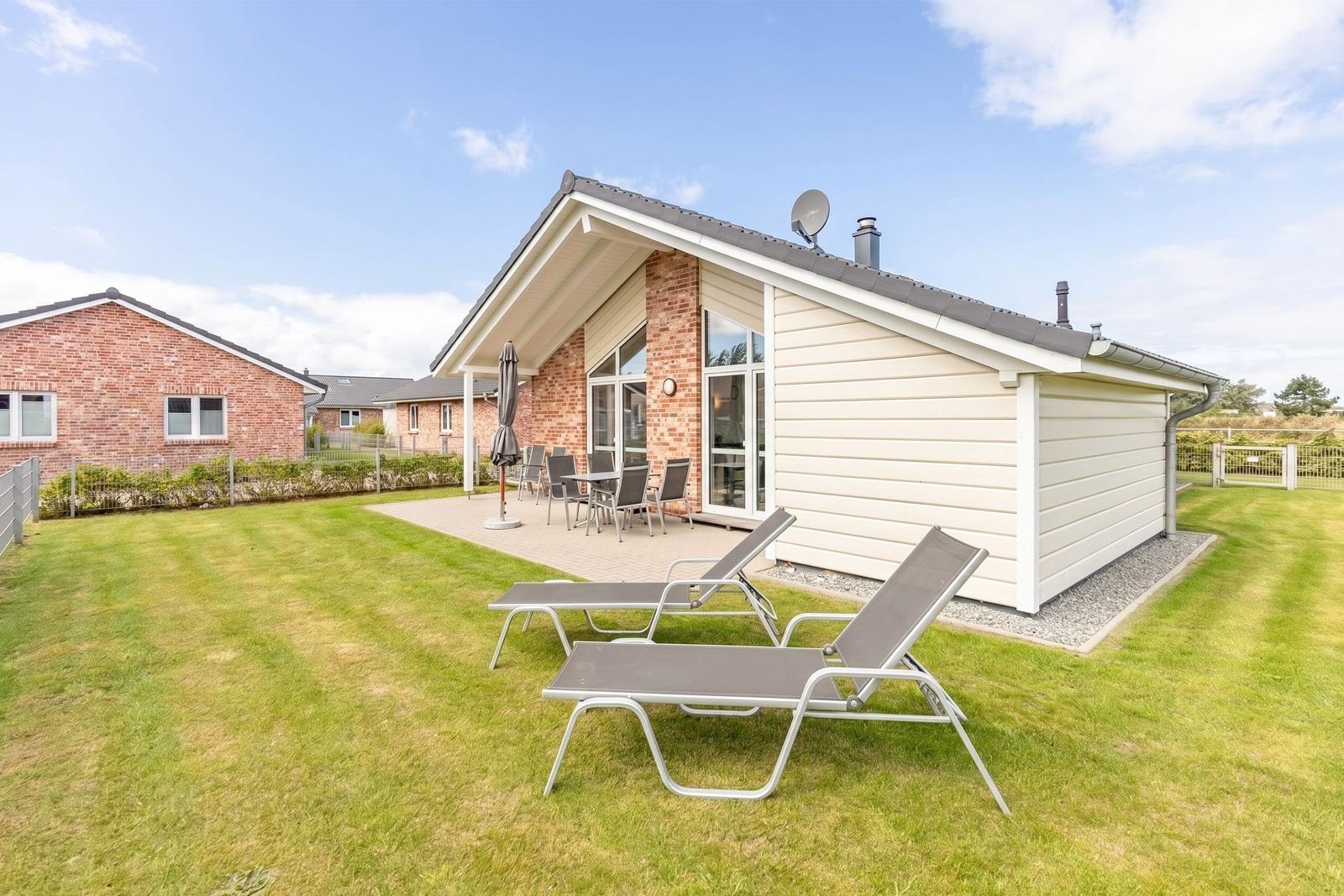 Haus mit Terrasse, Liegestühlen und Garten. Satellitenschüssel und Fenster sichtbar.