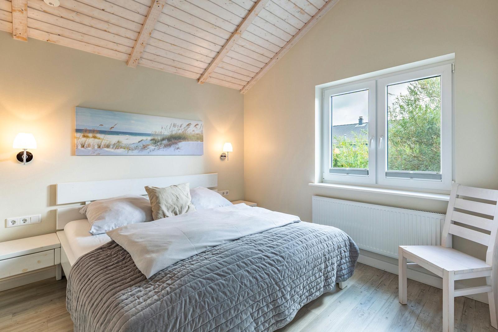 Schlafzimmer mit Bett, Fenster und Holzdecke. Wandbild und Stuhl sind sichtbar.