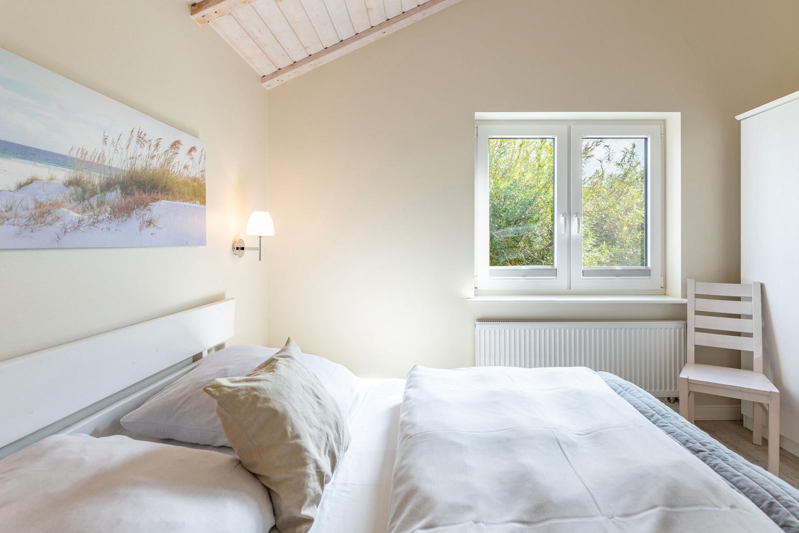 Schlafzimmer mit Bett, Fenster und Stuhl. Wandbild zeigt Strand.