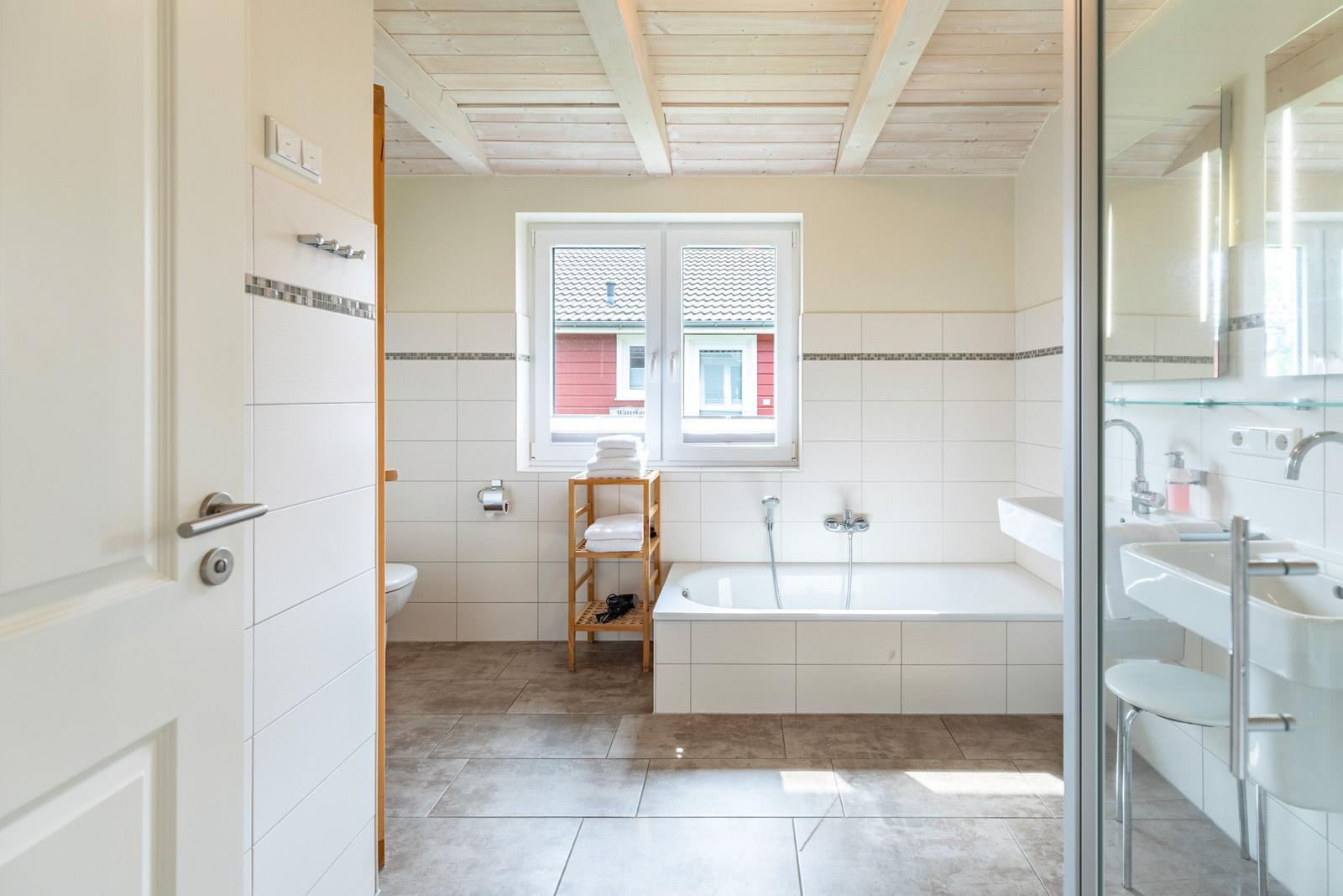 Badezimmer mit Badewanne, Waschbecken und Fenster. Holzdecke und Fliesen.