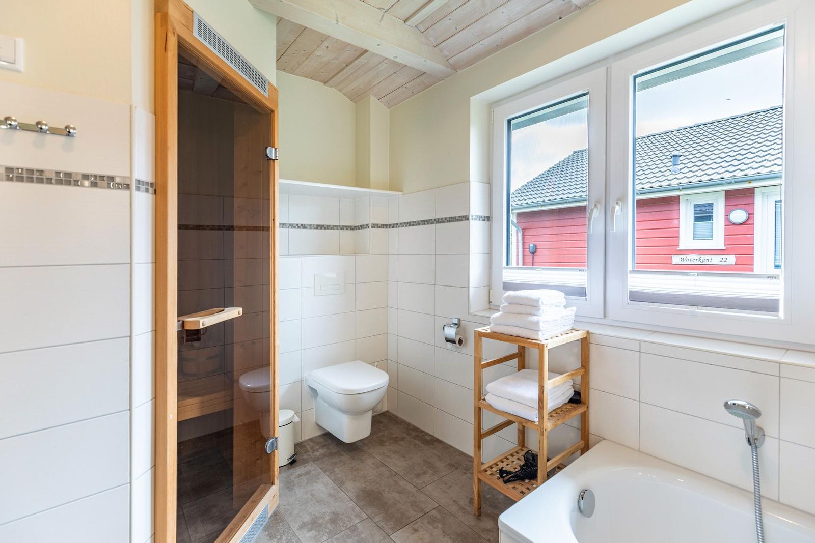Badezimmer mit Dusche, Badewanne und Fensterblick auf rotes Haus.
