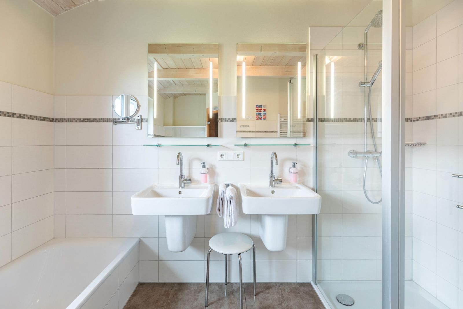 Badezimmer mit Dusche, Badewanne, zwei Waschbecken und Spiegeln.