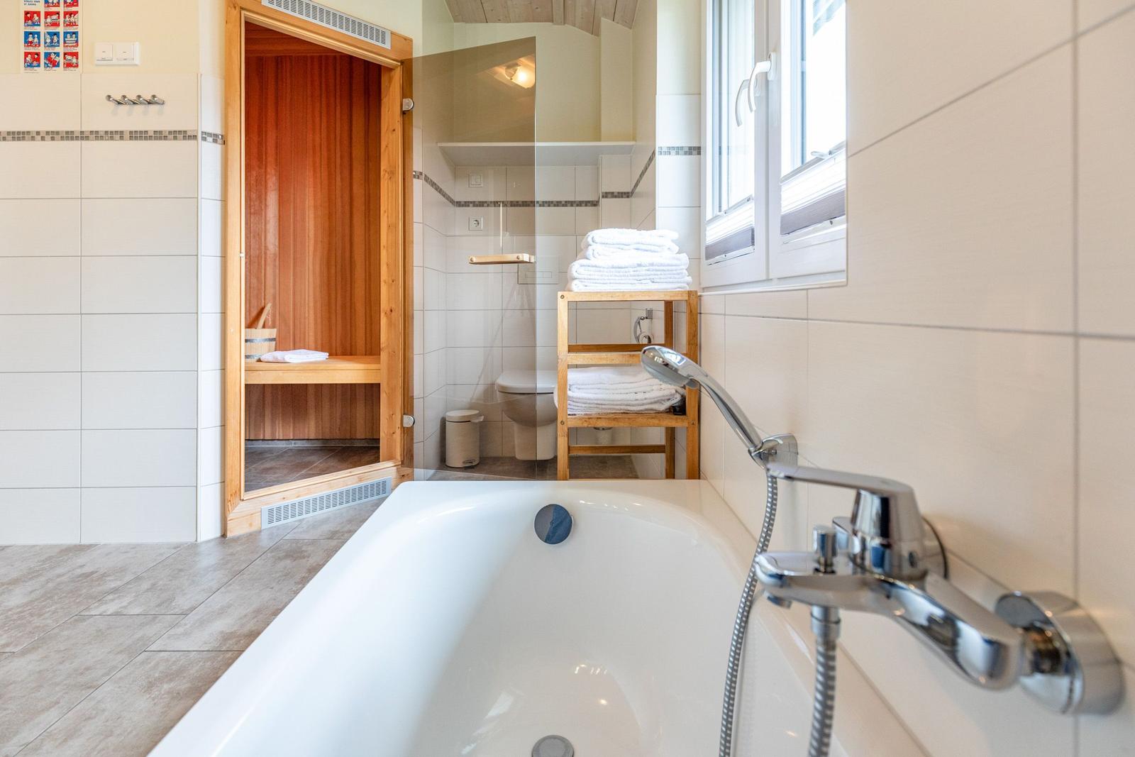 Bad mit Badewanne, Dusche, Toilette und Sauna. Handtuchständer und Fenster sichtbar.