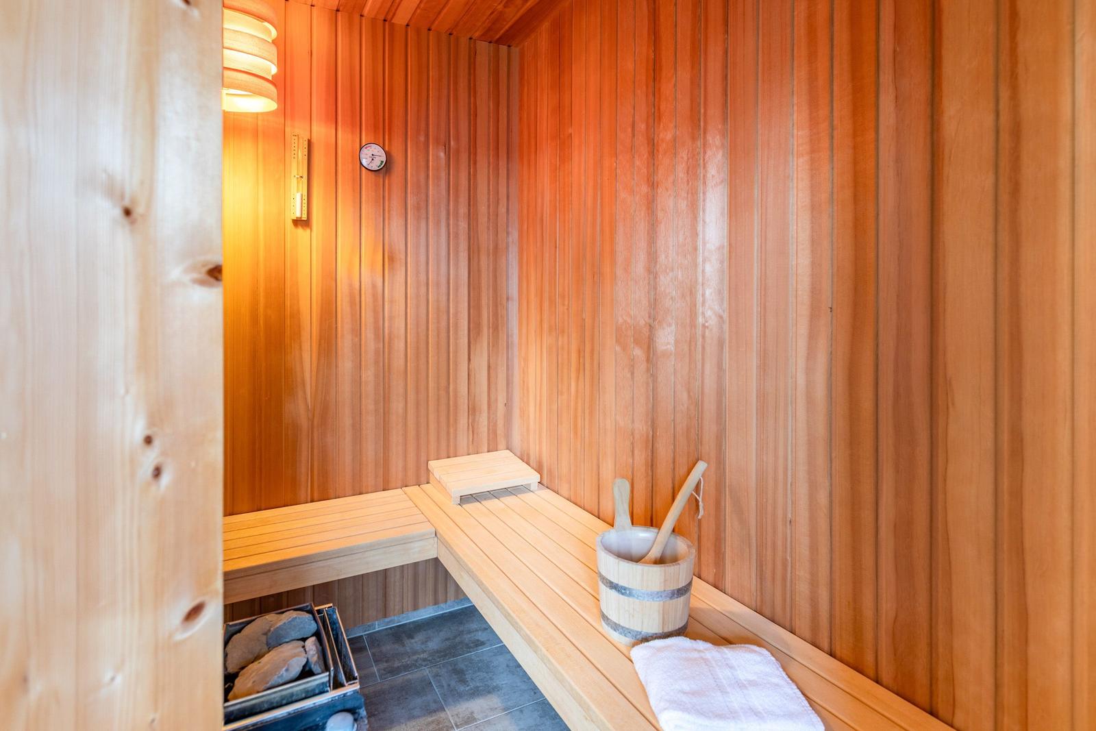 Sauna mit Holzwand, Sitzbank, Holzkrug und Handtuch.