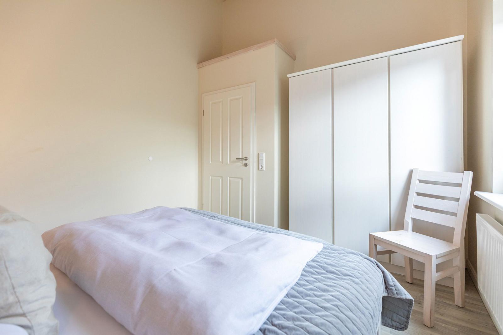 Schlafzimmer mit Bett, Kleiderschrank und Stuhl.
