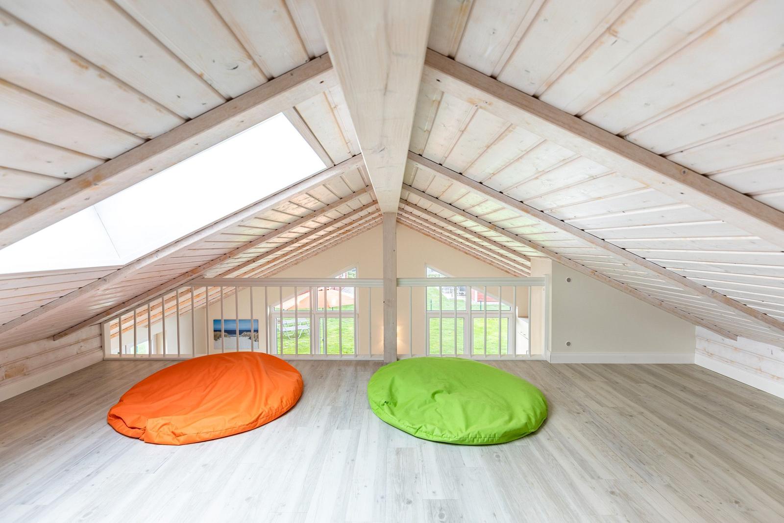 Zwei farbige Sitzkissen auf Holzboden unter Dachschräge mit Fenster und Balkon.