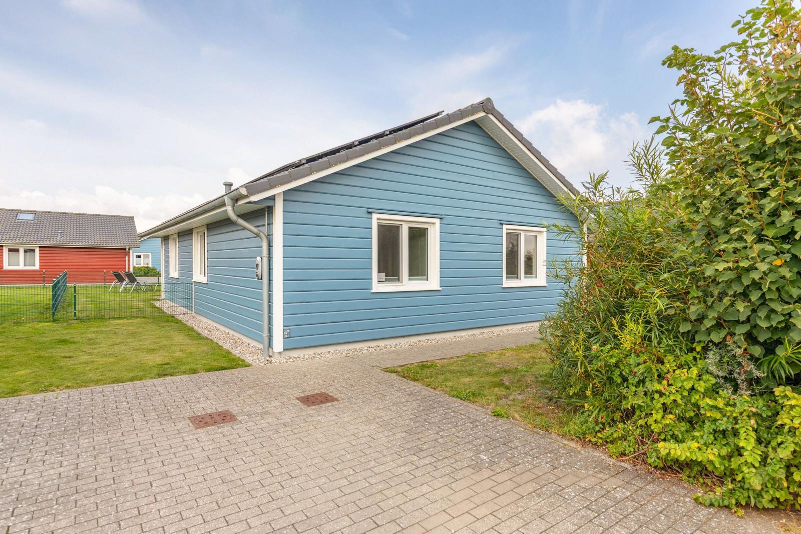 Ein blaues Haus mit weißen Fenstern und einem gepflasterten Vorplatz.