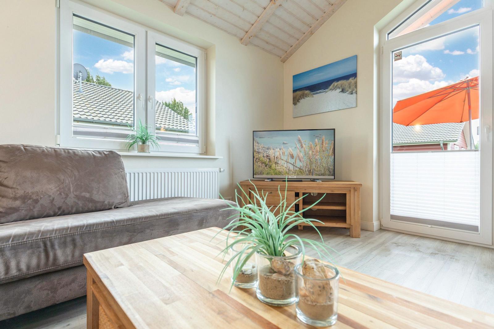 Wohnzimmer mit Sofa, TV und Blick auf Balkon mit Sonnenschirm.