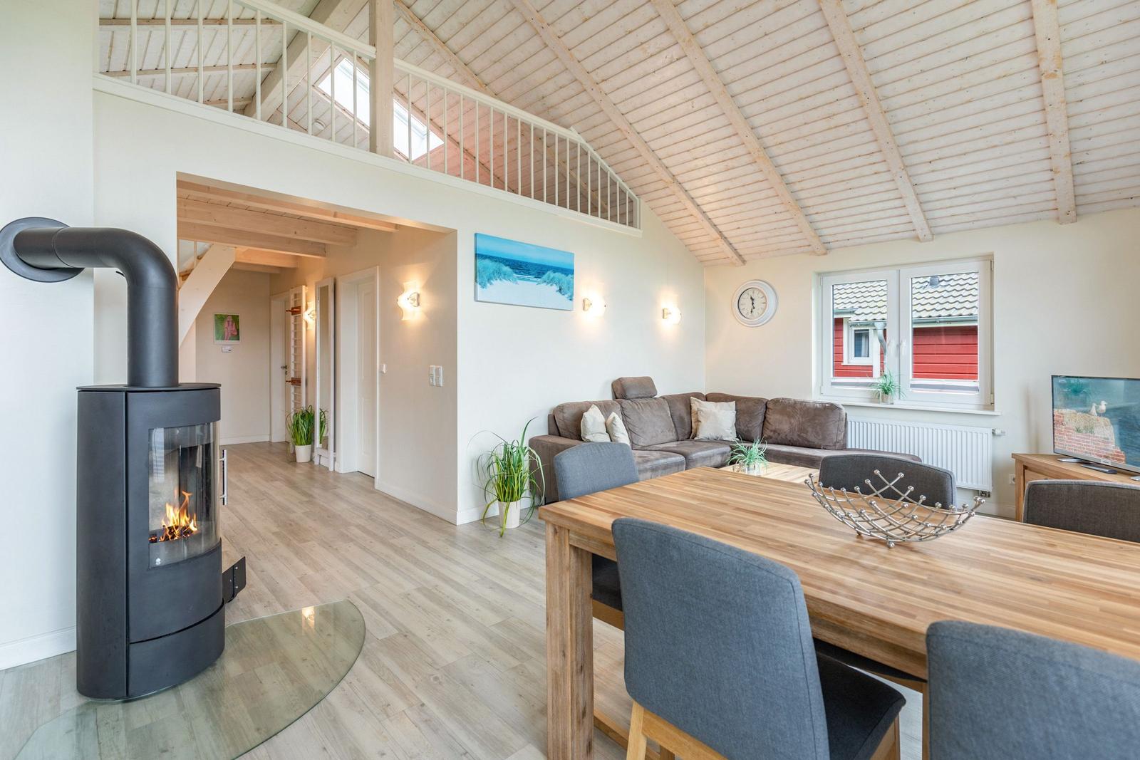 Wohn- und Essbereich mit Kamin, Sofa und Holztisch. Obergeschoss mit Balkon.