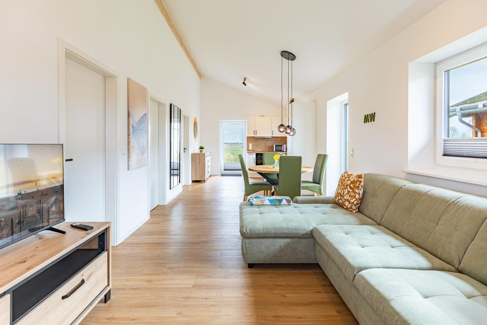 Wohnzimmer mit Sofa, Fernseher und Blick in die Küche