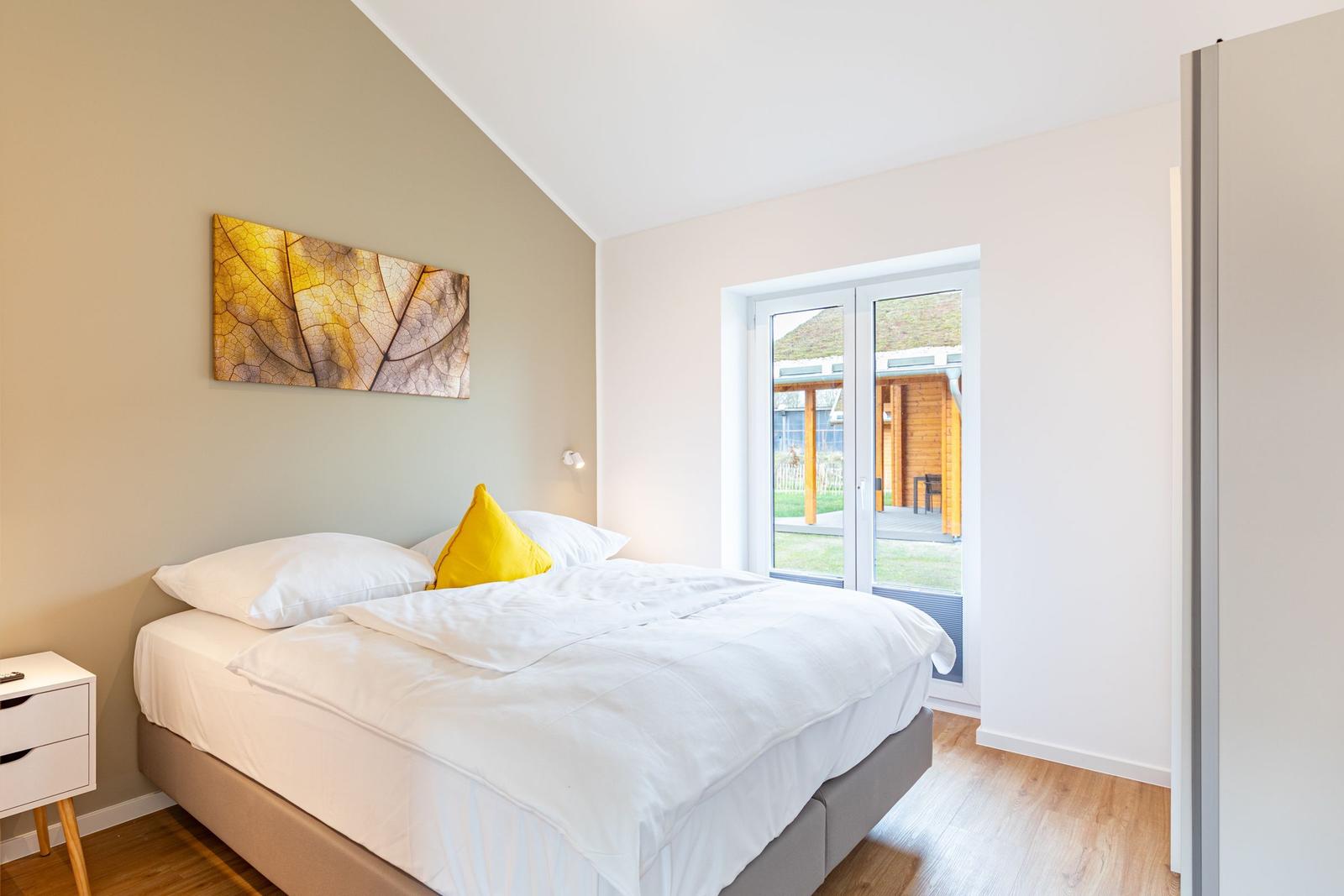 Schlafzimmer mit Bett, Nachttisch und Fenster zur Terrasse.