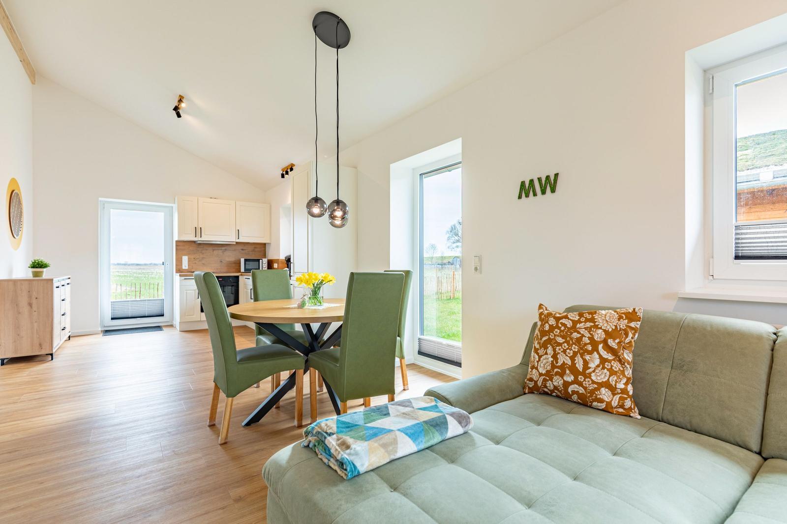 Wohn- und Essbereich mit Sofa, Tisch und Stühlen. Fenster mit Blick auf die Landschaft.