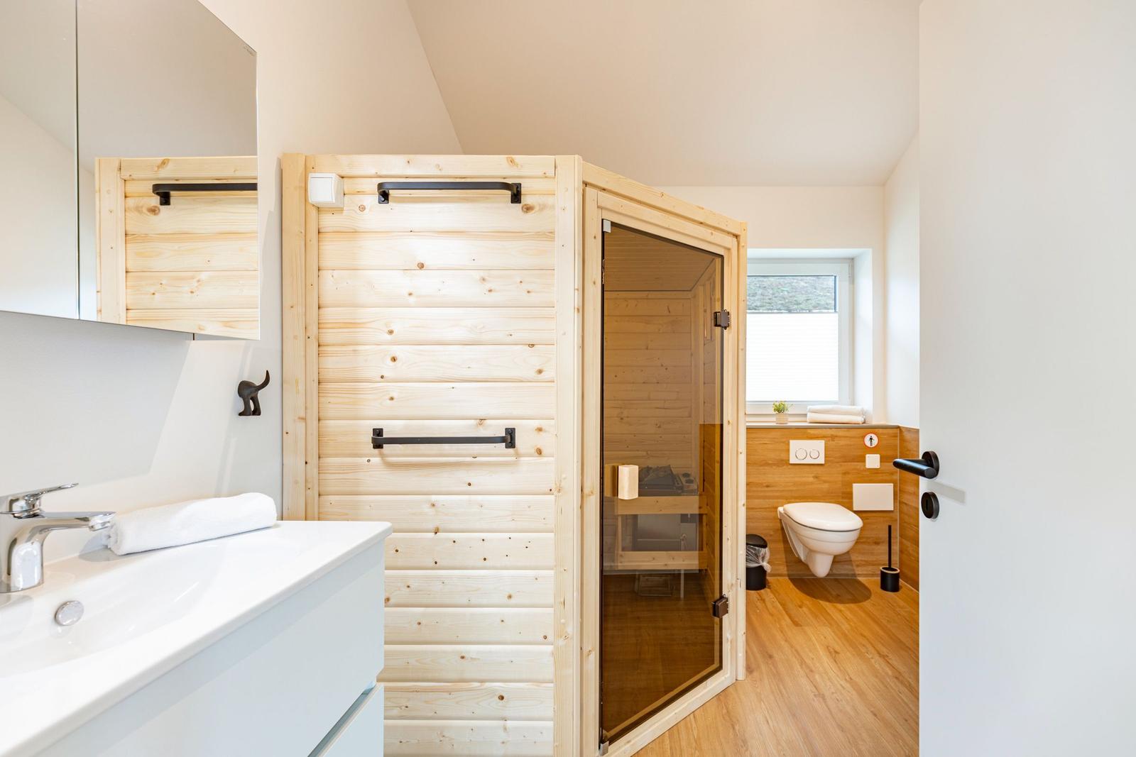 Badezimmer mit Holzsauna, Waschbecken und WC. Holzfußboden und Fenster.