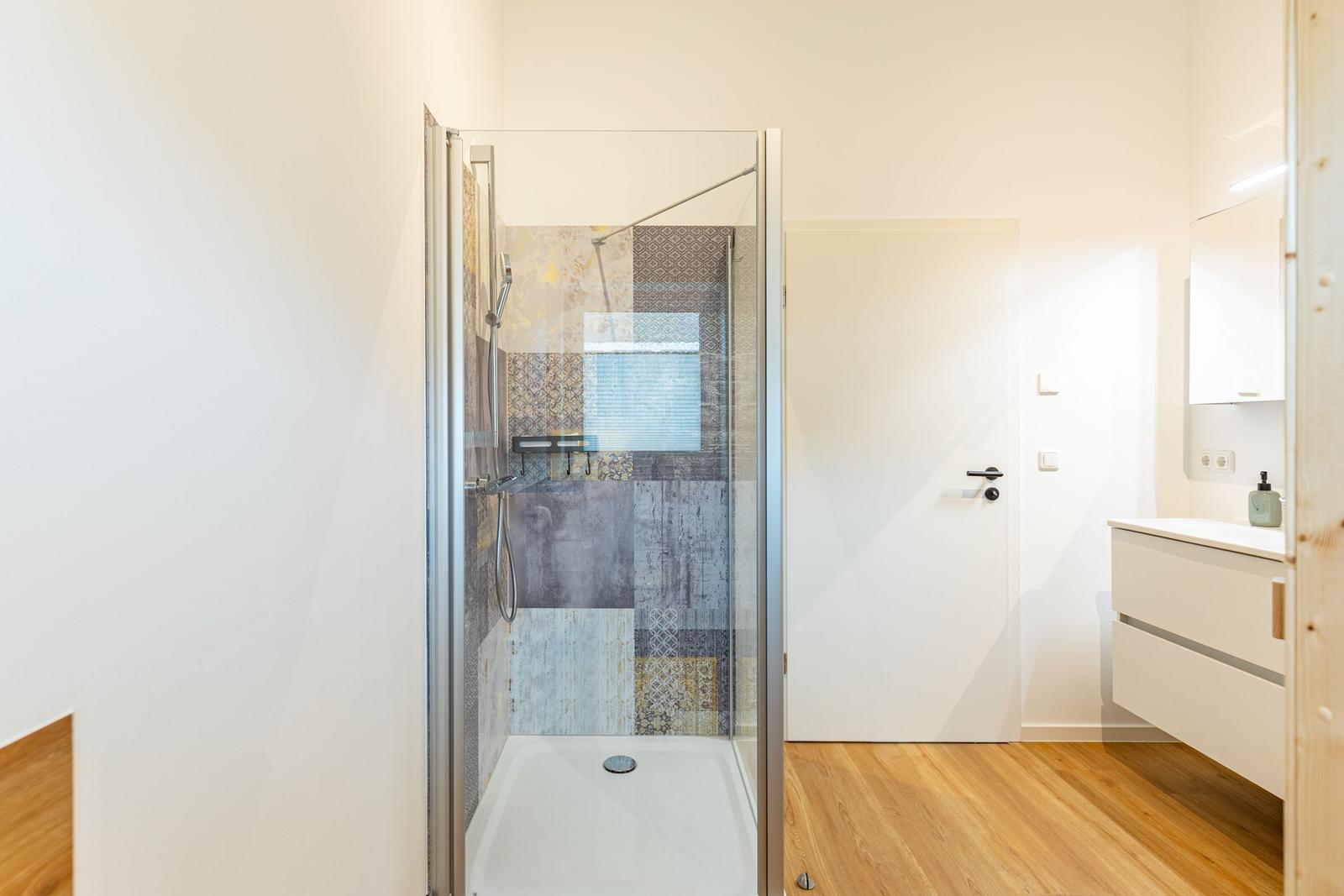 Dusche mit Glaswand, Fliesenwand und Waschbecken mit Spiegelschrank.