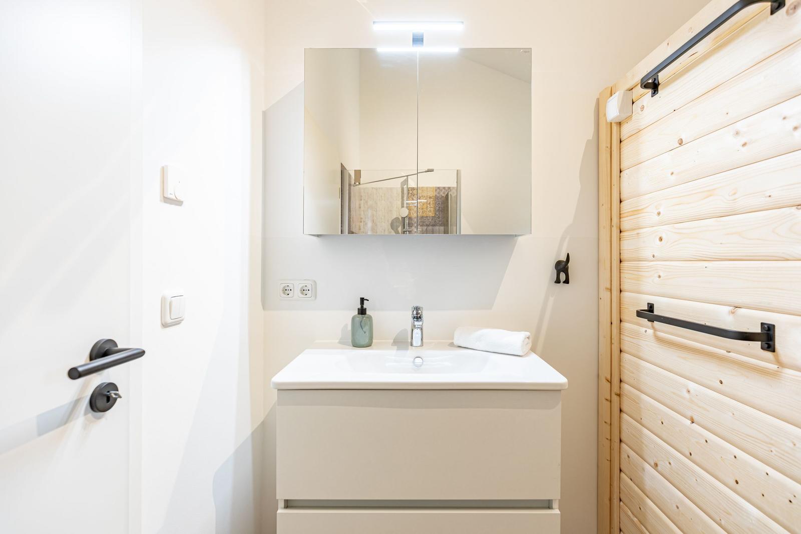 Badezimmer mit Waschbecken, Spiegel und Holzwand