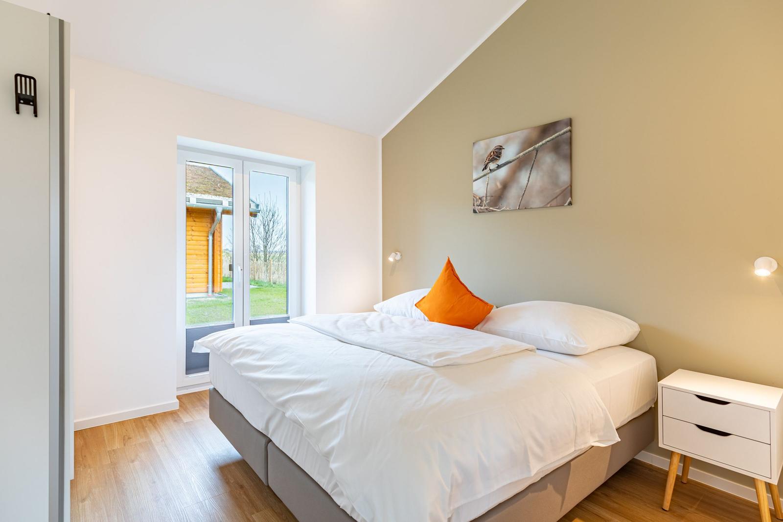 Schlafzimmer mit Bett, Nachttisch und Fenster zur Außenterrasse.