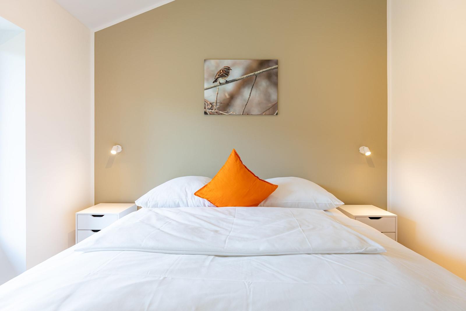 Schlafzimmer mit Bett, zwei Nachttischen und Wandbild eines Vogels.