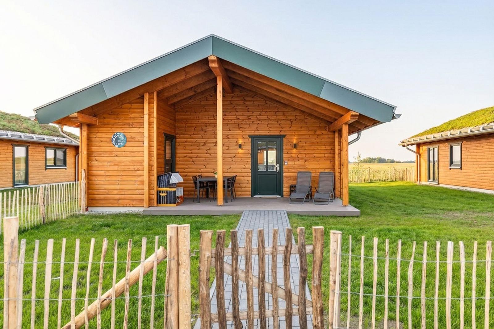 Holzhaus mit Terrasse, Garten und Holzzaun. Tür und Fenster sind dunkel.