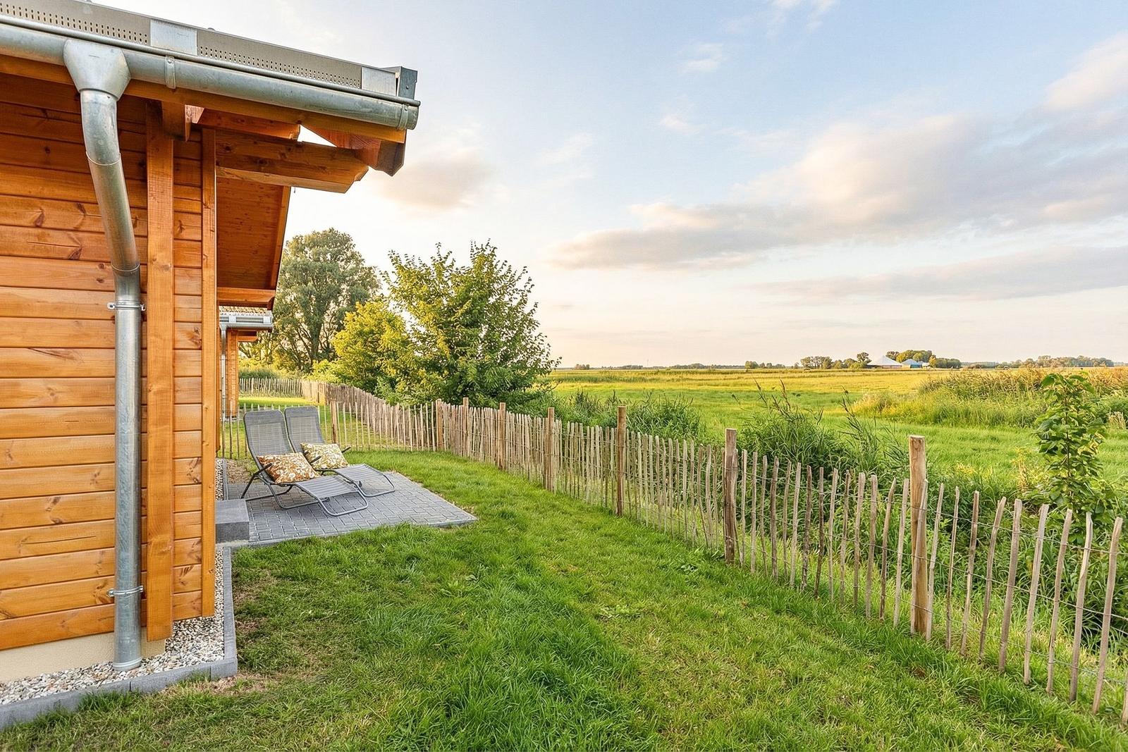 Holzhaus mit Terrasse, Liegestühle und Blick auf grünes Feld.