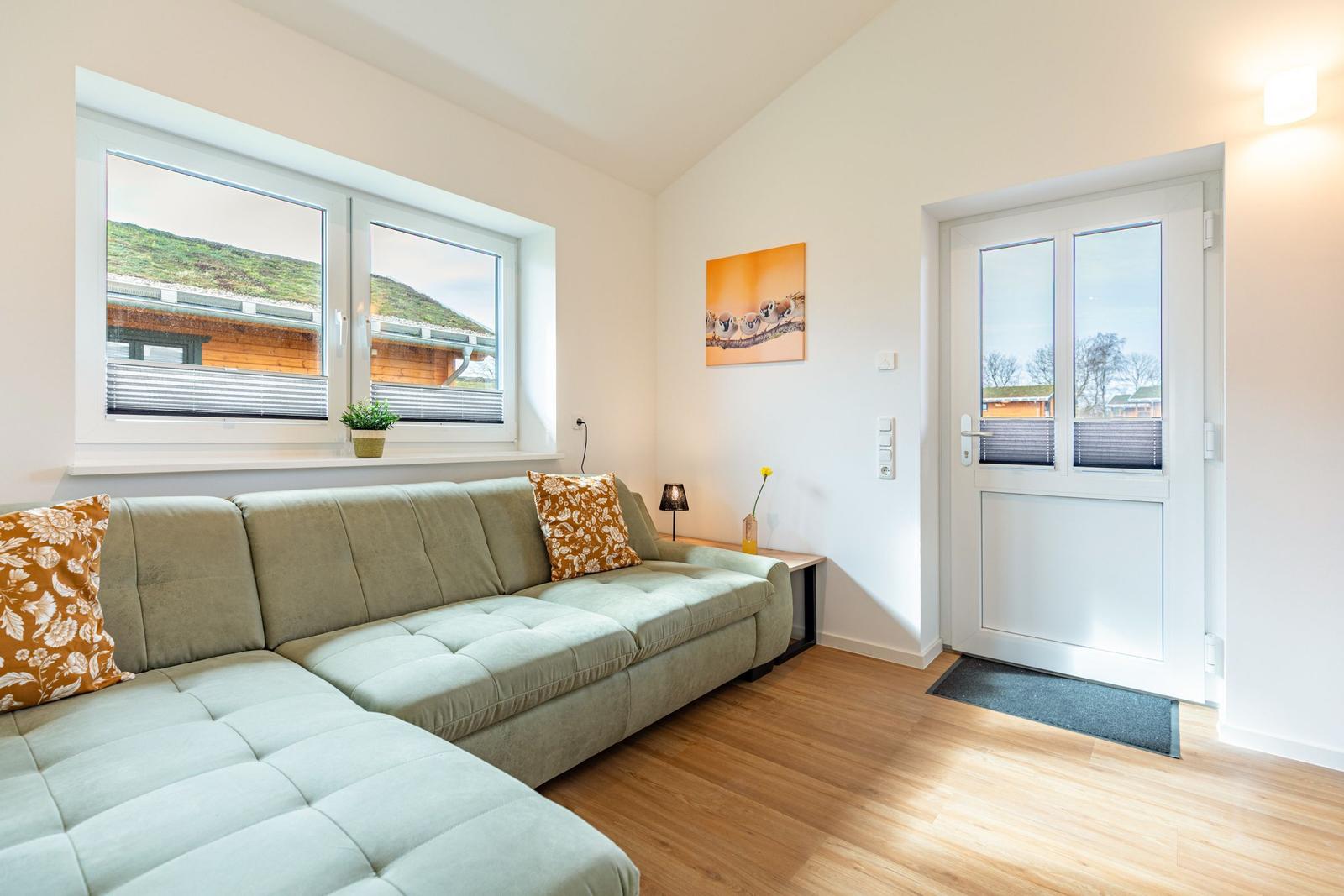 Wohnzimmer mit Sofa, Fenster und Tür. Holzboden und Wandbild.