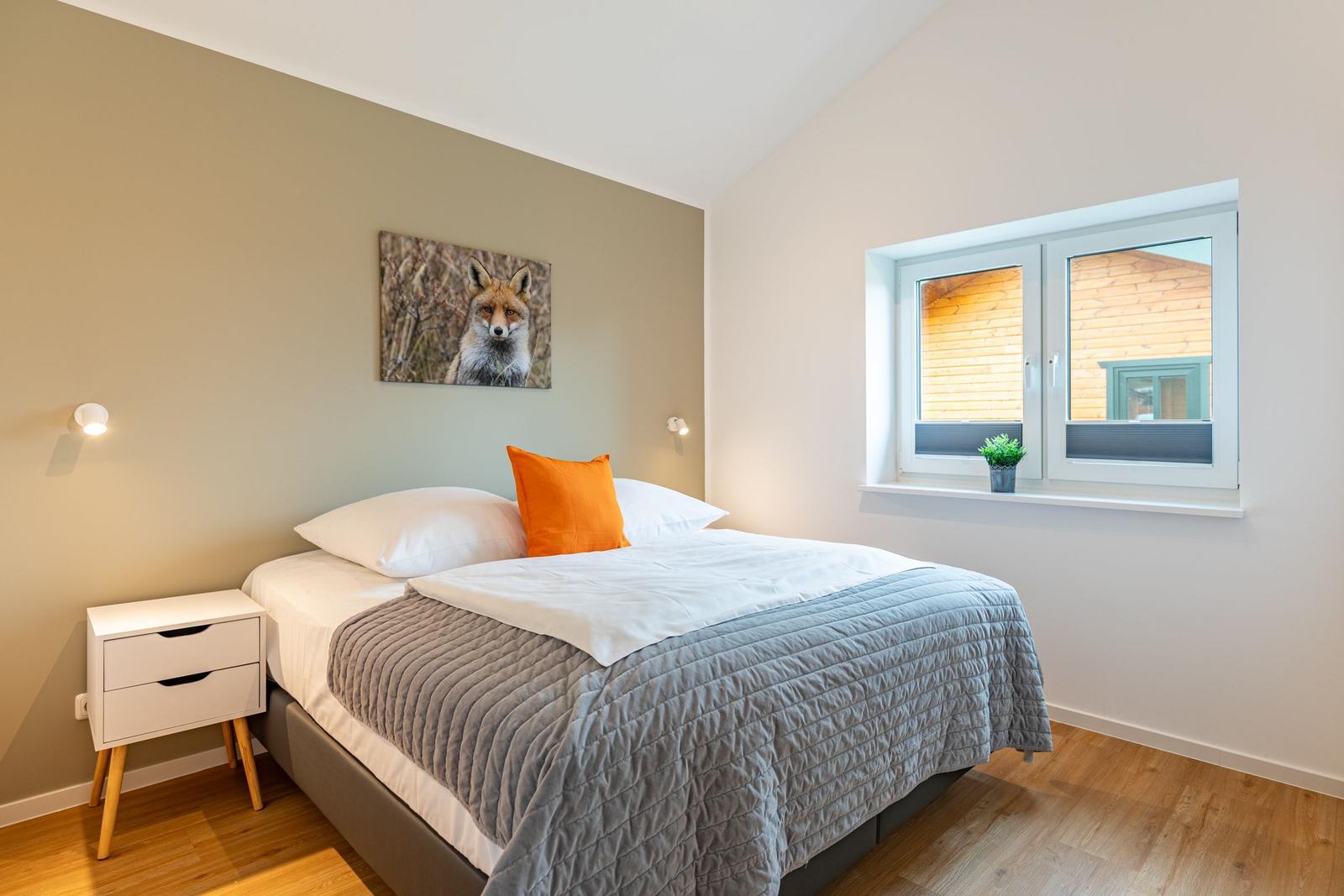 Schlafzimmer mit Bett, Nachttisch und Fenster. Wandbild eines Fuchses.