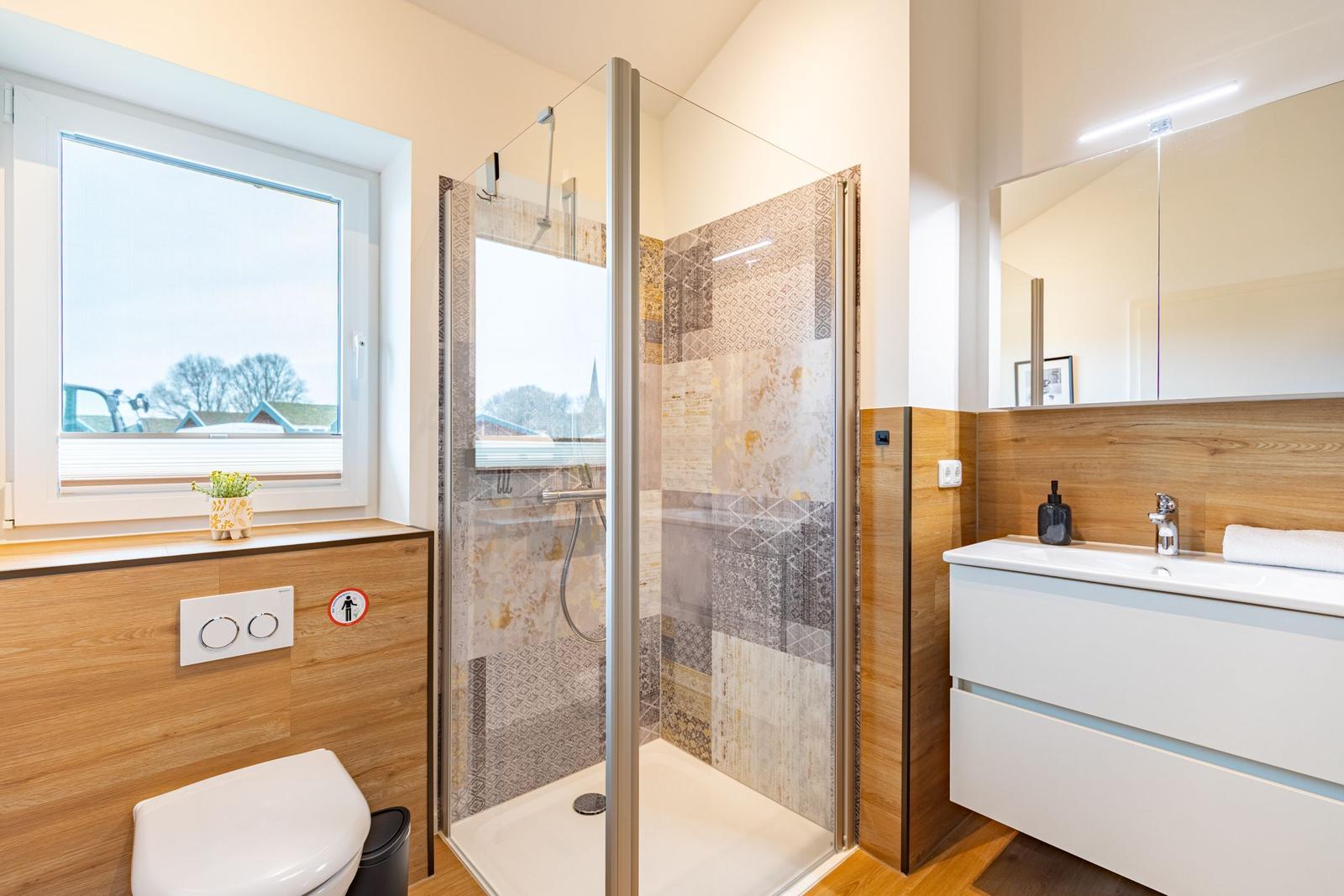 Bad mit Dusche, Waschbecken und Toilette. Fenster mit Blick nach draußen.