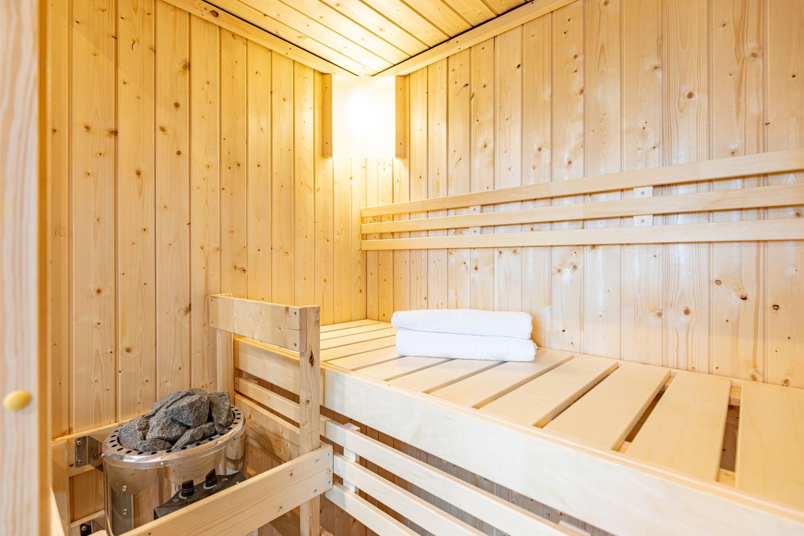 Sauna mit Holzwand und -bänken, Steinkessel und gefalteten Handtüchern.