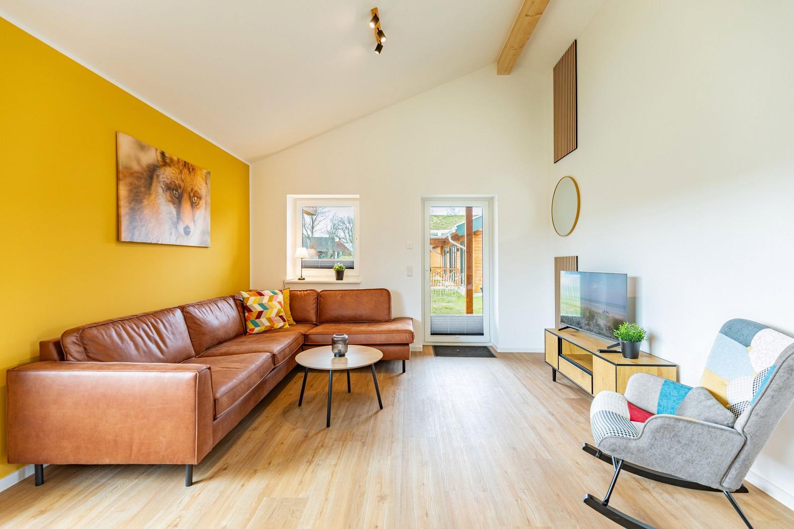 Wohnzimmer mit braunem Sofa, gelber Wand und Fernseher.