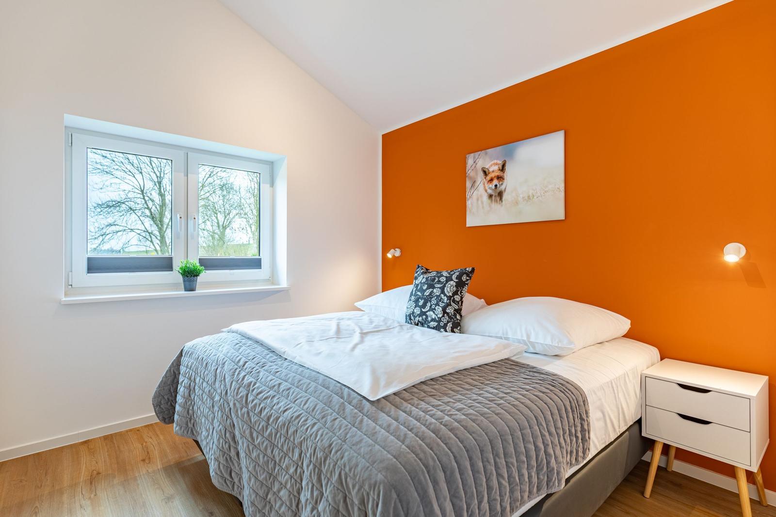 Schlafzimmer mit Bett, Fenster und orangeer Wand. Wandbild zeigt einen Fuchs.