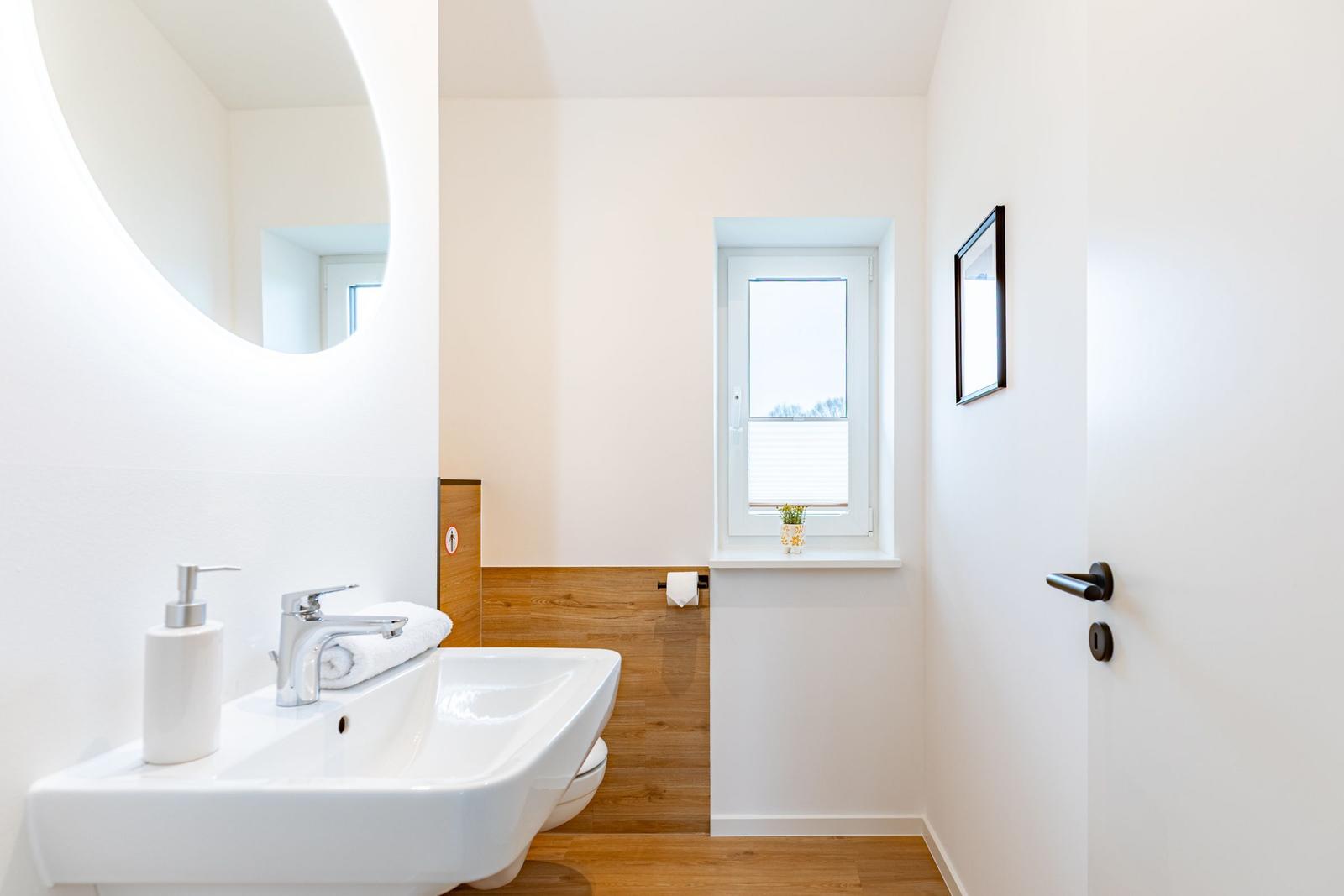 Badezimmer mit Waschbecken, Spiegel, Toilette und Fenster.