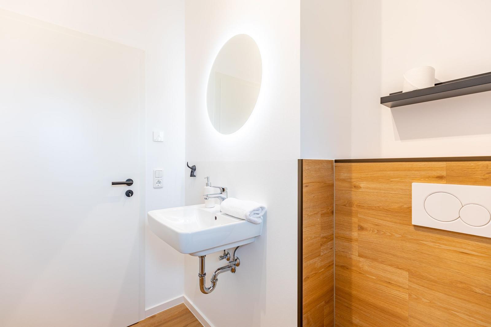 Badezimmer mit Waschbecken, runden Spiegel und Holzwandverkleidung.