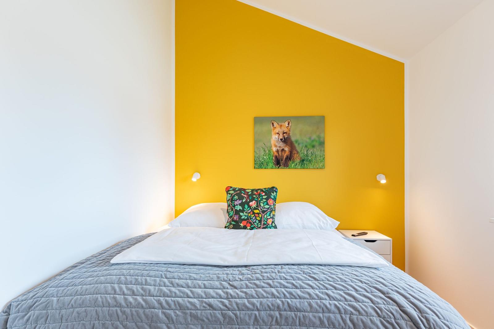 Schlafzimmer mit gelber Wand, Bett und Wandbild eines Fuchses.