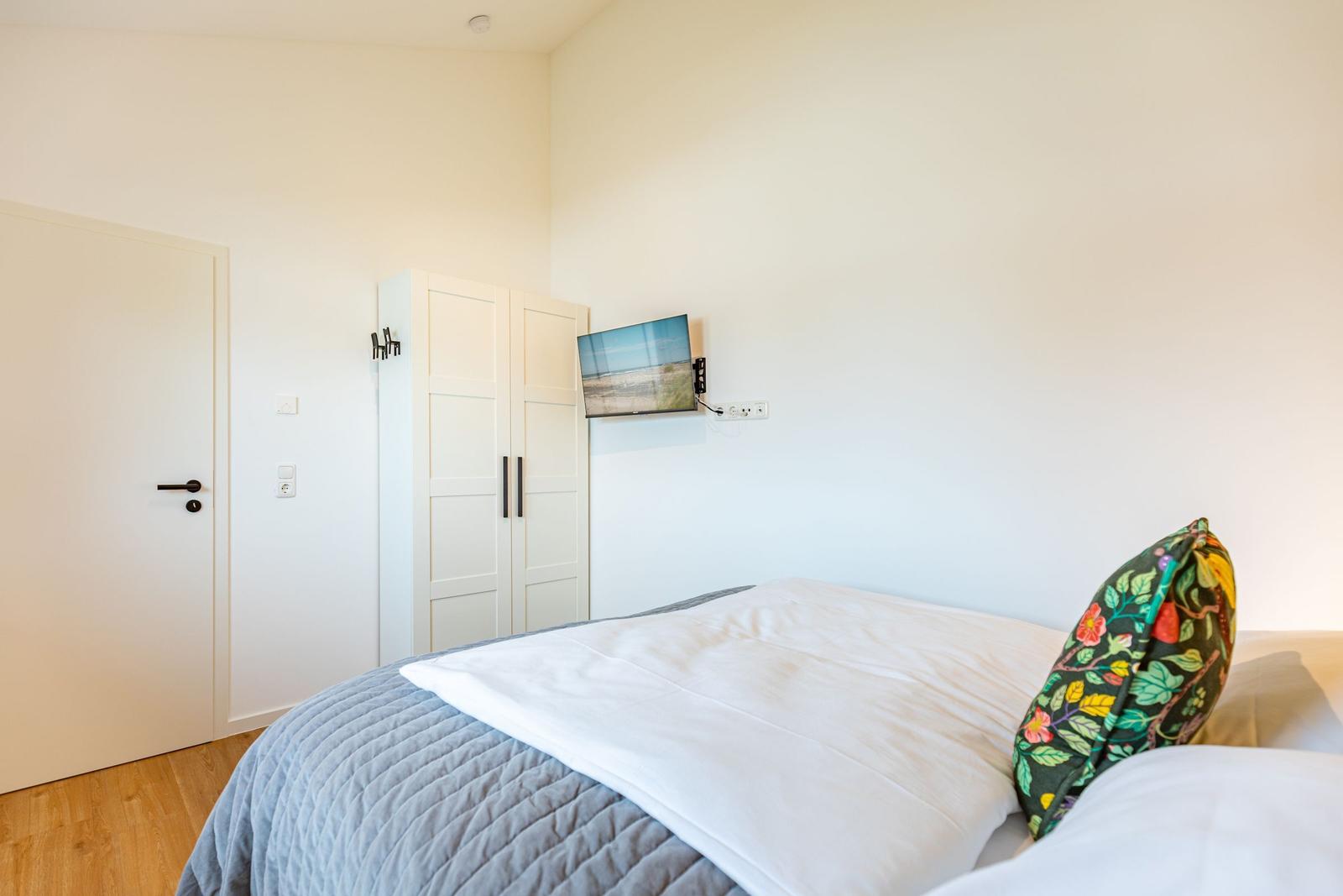 Schlafzimmer mit Bett, Kleiderschrank und Wand-TV.