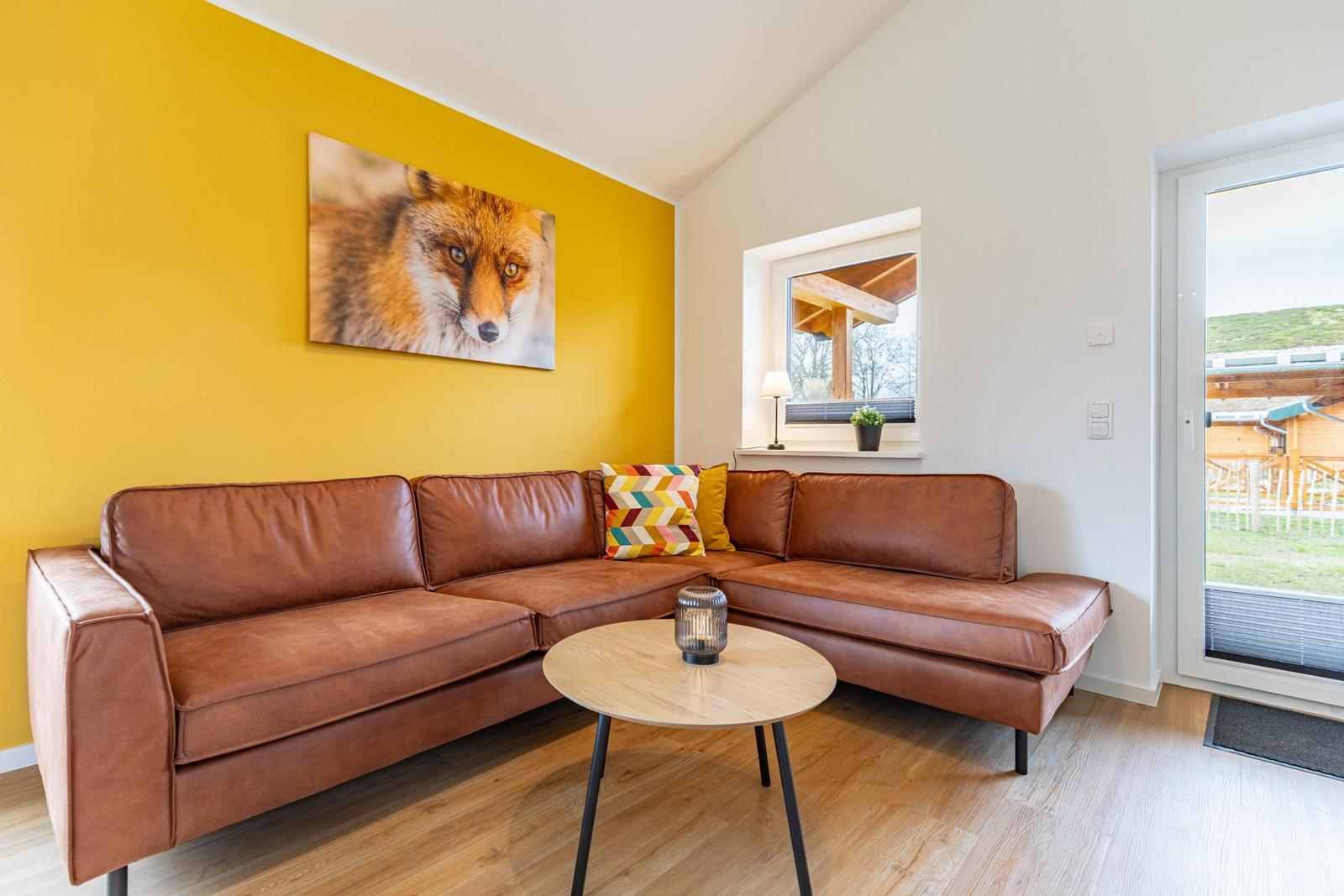 Ein Wohnzimmer mit braunem Sofa, gelber Wand und Wandbild eines Fuchses.