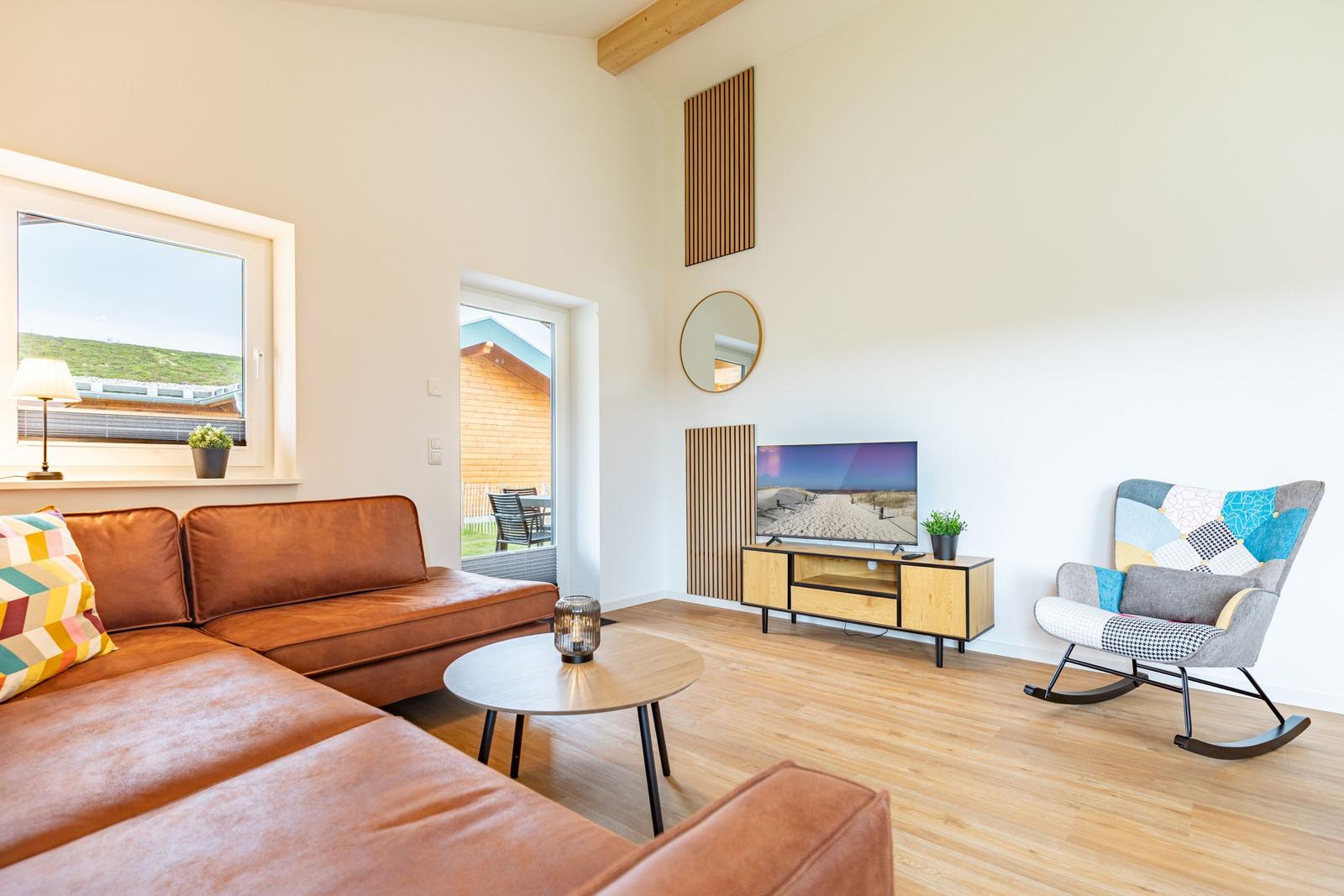 Wohnzimmer mit braunem Sofa, Schaukelstuhl und Fernseher auf Holzregal.