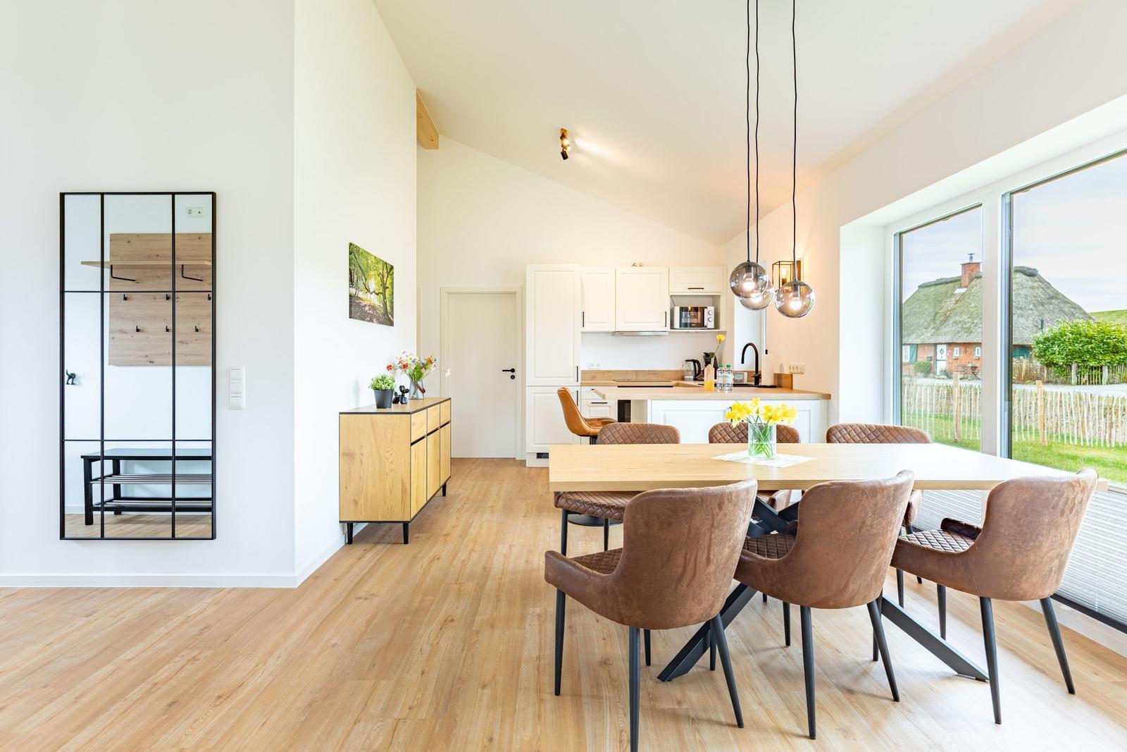 Essbereich mit Holztisch und braunen Stühlen. Küche und Wohnbereich mit Holzboden und großen Fenstern.