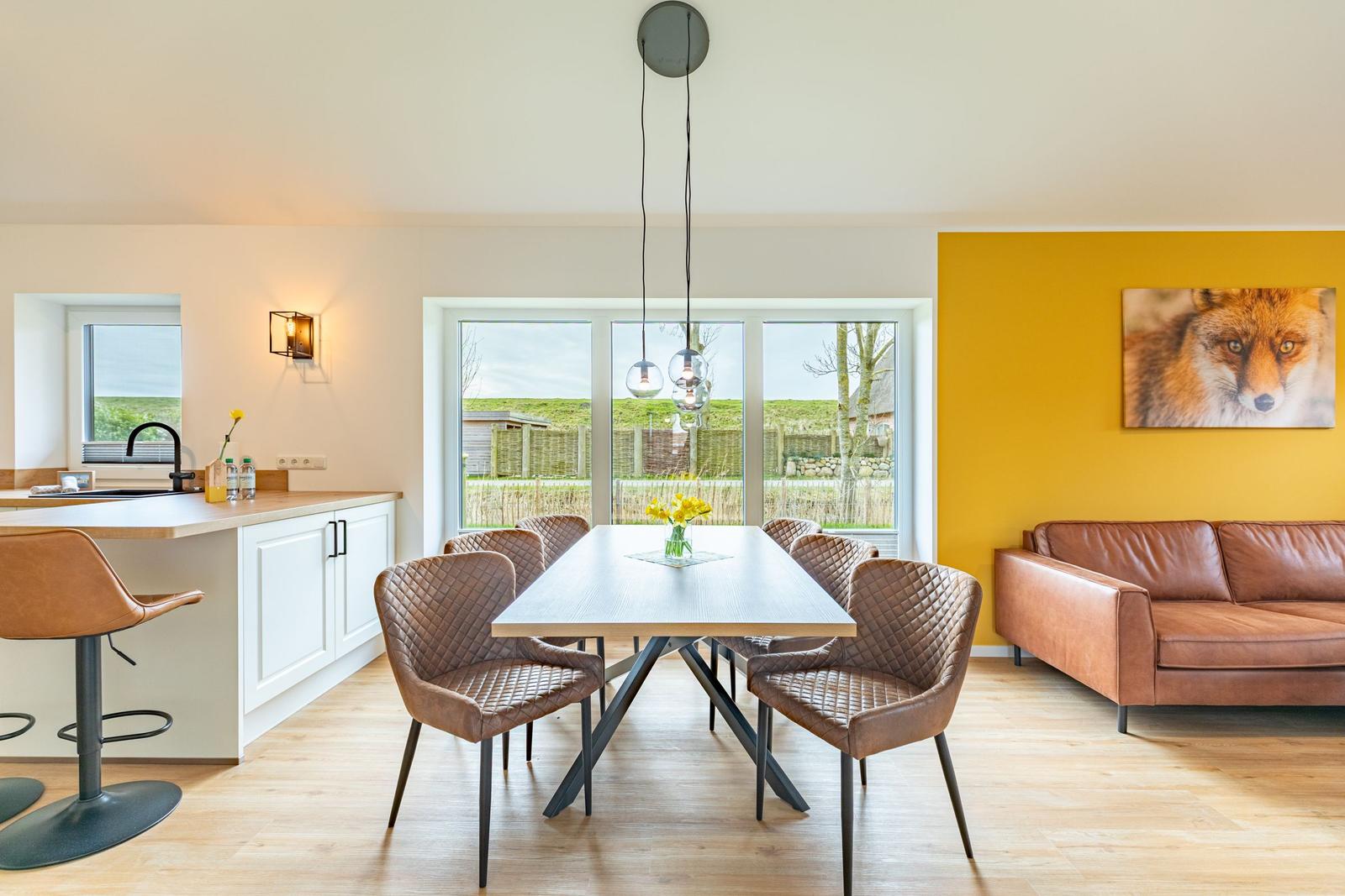 Essbereich mit Tisch und Stühlen, Küchenzeile und Sofa an gelber Wand mit Fuchsbild.