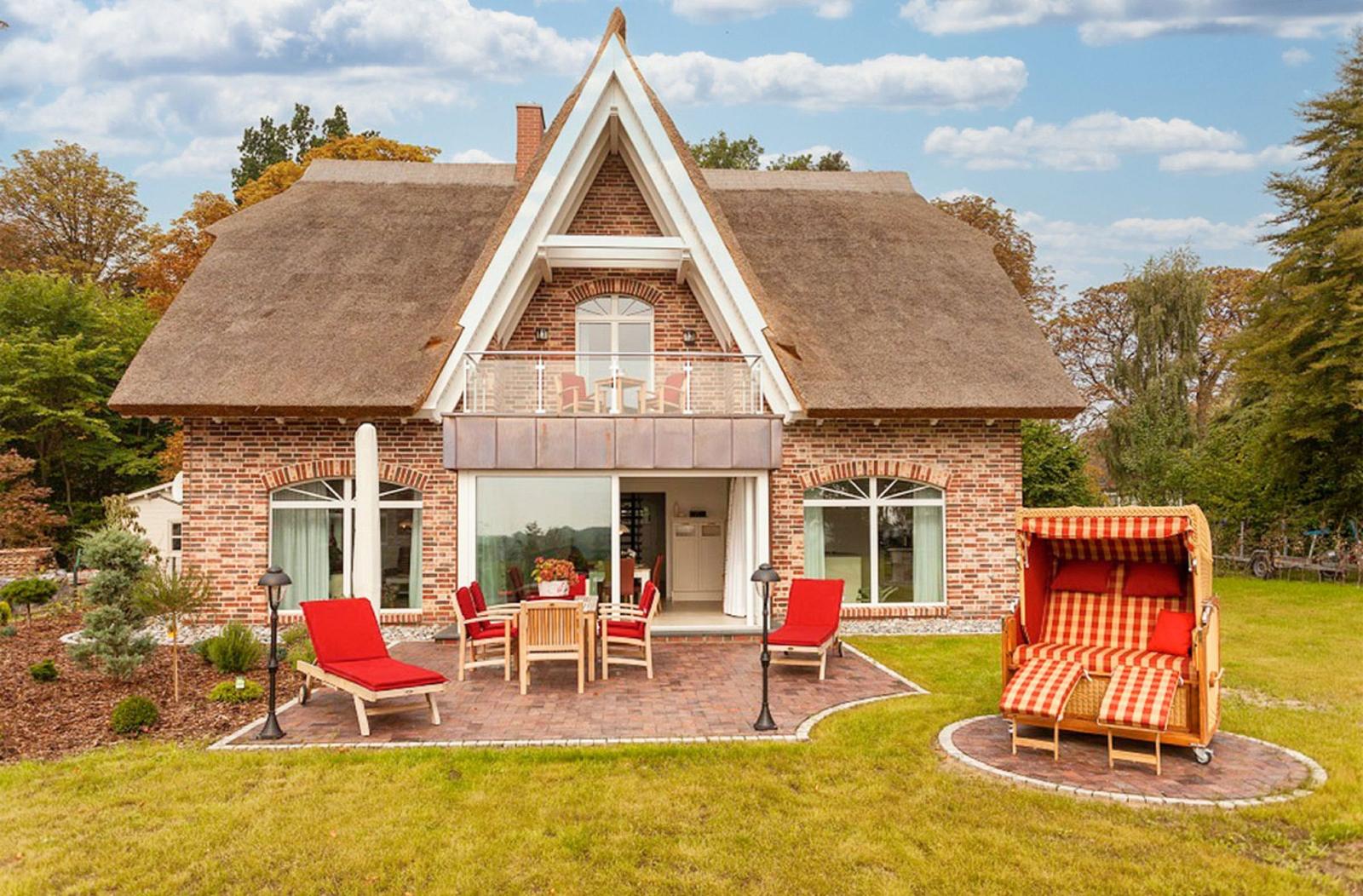 Rotes Gartenmöbel und Strandkorb vor einem Haus mit Strohdach und Balkon.