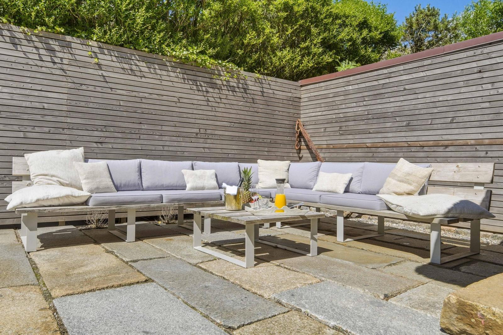 Terrasse mit Sitzgruppe, Tisch und Steinplatten. Holzwand im Hintergrund.
