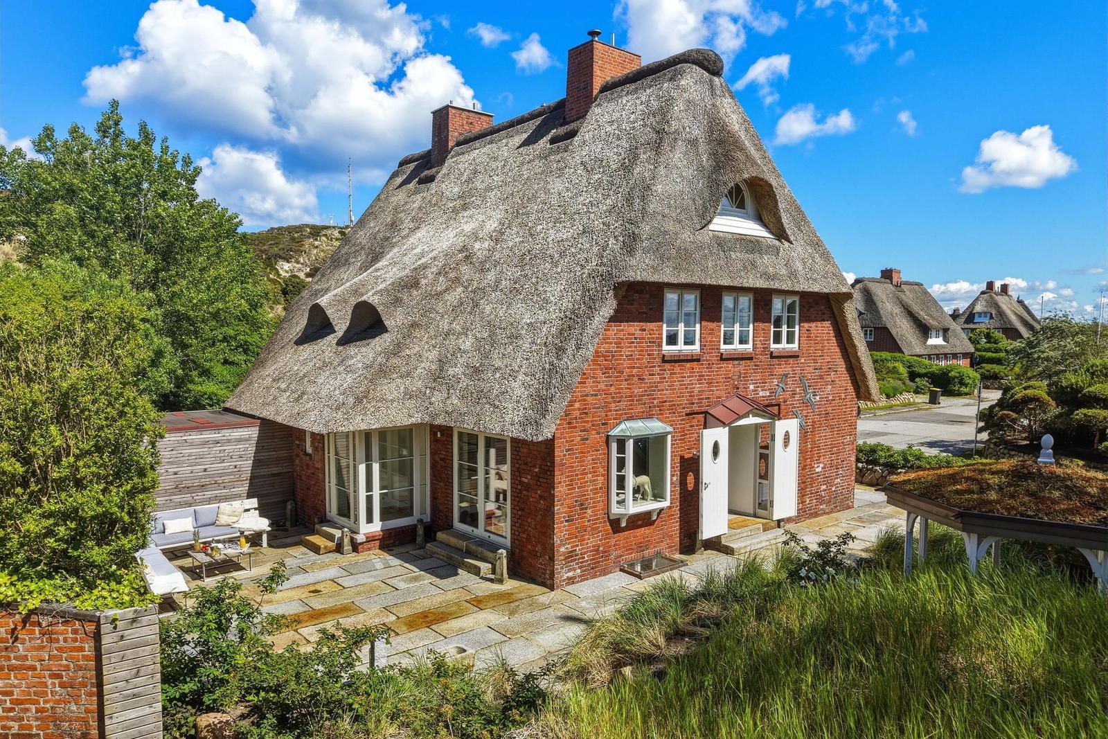 Rotes Backsteinhaus mit Strohdach und Terrasse im Freien.