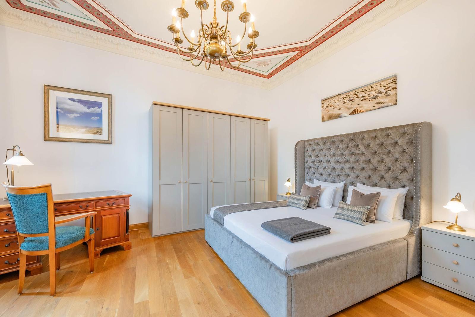 Schlafzimmer mit Bett, Schreibtisch, Kleiderschrank und Kronleuchter.