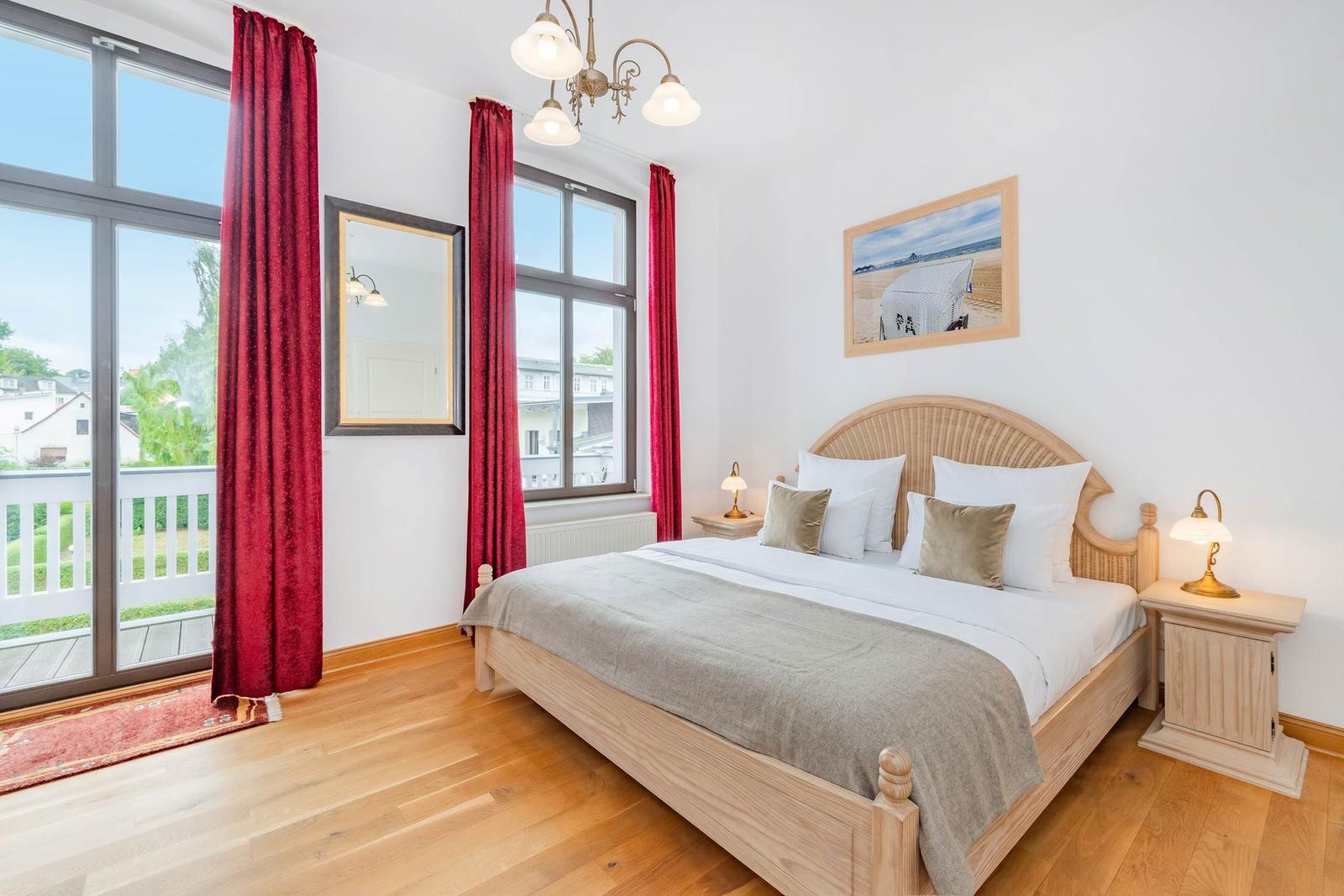Schlafzimmer mit Holzbett, roten Vorhängen und Blick auf Balkon.