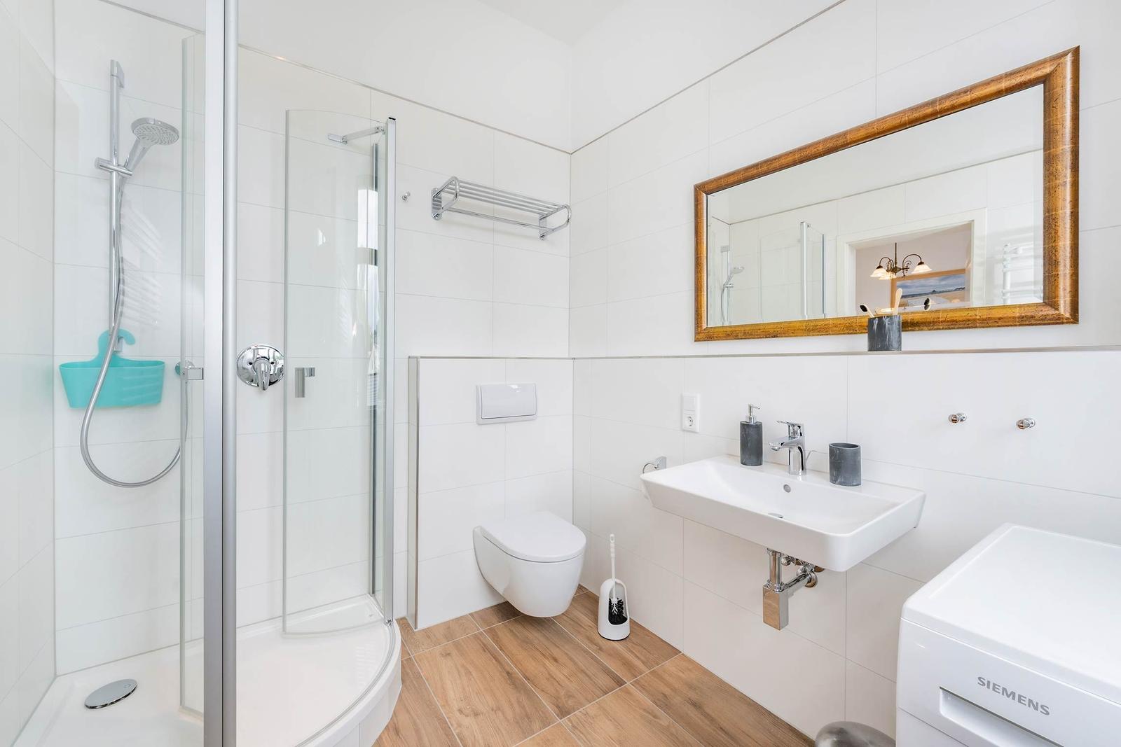 Badezimmer mit Dusche, Waschbecken und Toilette. Holzoptik Boden. Spiegel mit Holzrahmen.