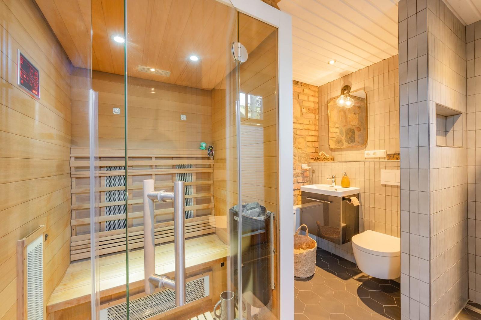 Sauna mit Holzwand und Glasfront. Nebenraum mit Waschbecken, Toilette und Steinwand.