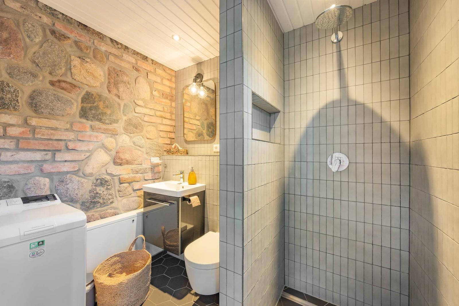 Bad mit Dusche, Waschbecken und Toilette. Steinwand und Fliesen.