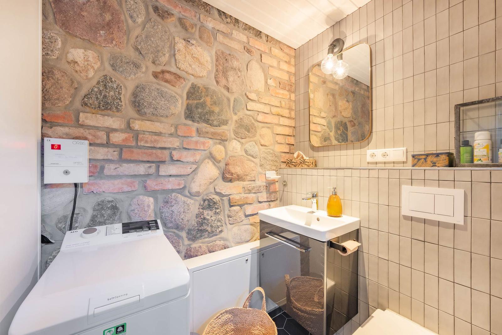 Badezimmer mit Steinwand, Waschmaschine und Spiegel